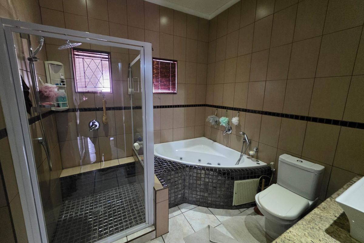 A functional bathroom featuring a corner jetted bathtub, a glass-enclosed shower, and a standard toilet with full-height wall tiling.