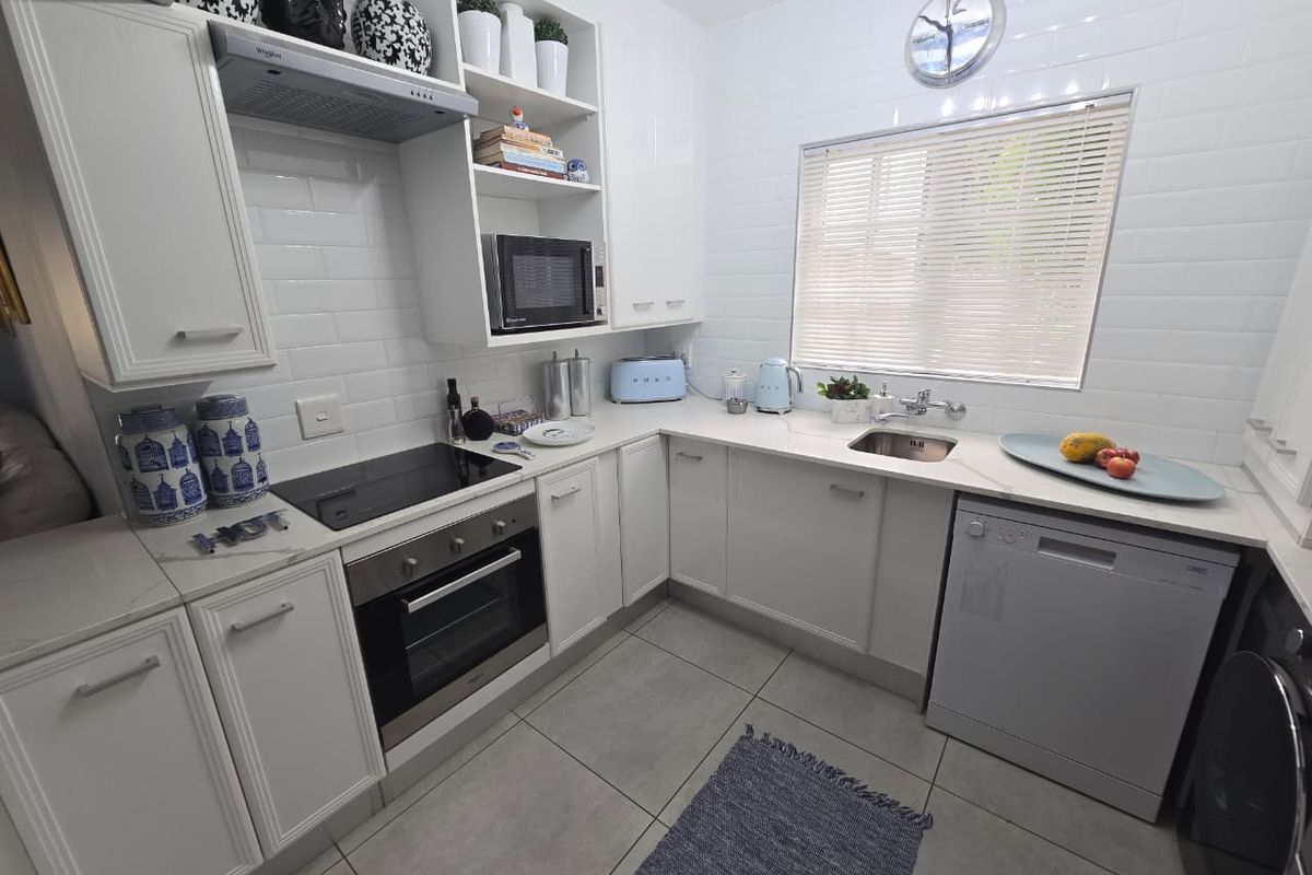 Modern kitchen featuring white cabinetry, subway tile backsplash, stone countertops, built-in oven, electric hob, extractor fan, and integrated sink with window view.