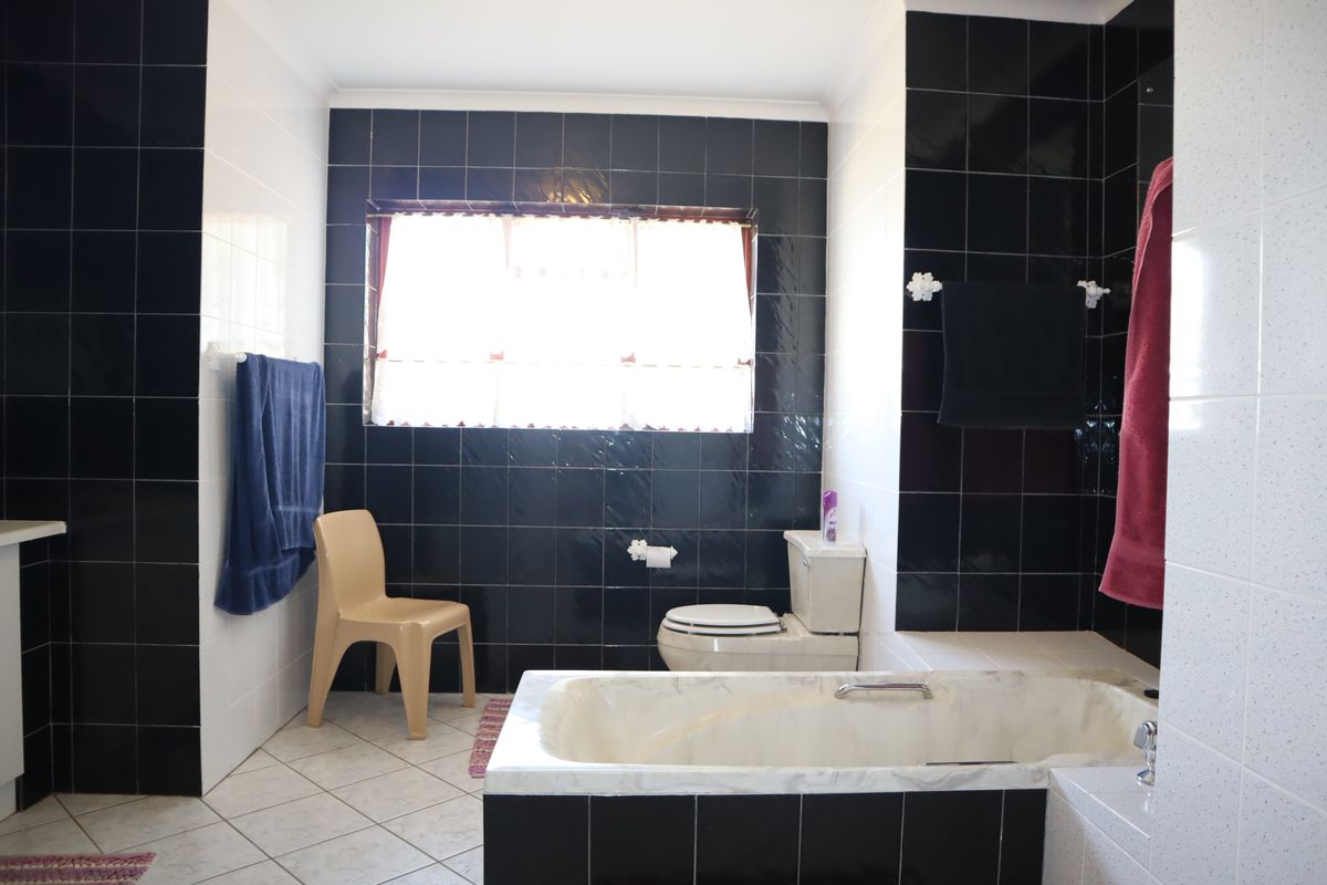A bathroom featuring a built-in bathtub with black tiled surround, a standard toilet, and contrasting black and white wall tiling.