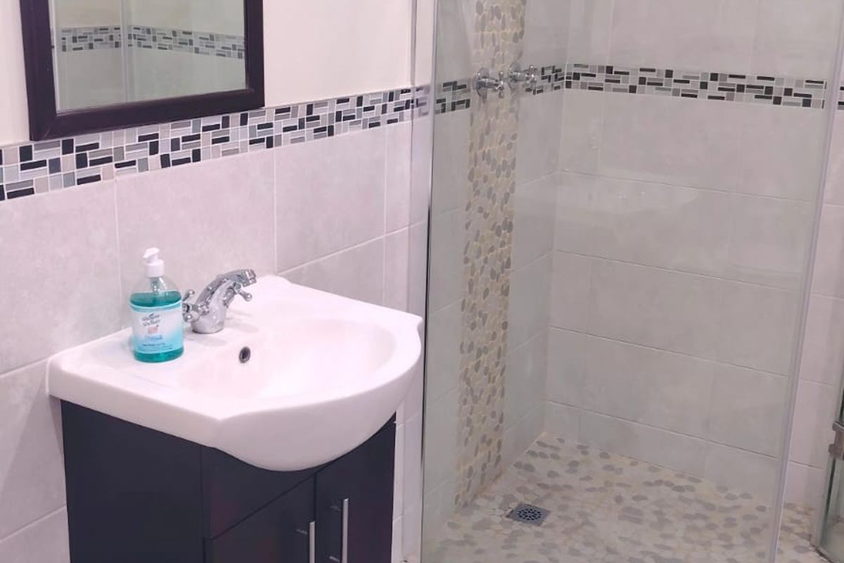 Modern bathroom featuring a vanity cabinet with basin, a walk-in shower with a rain shower head, and decorative mosaic tile accents.