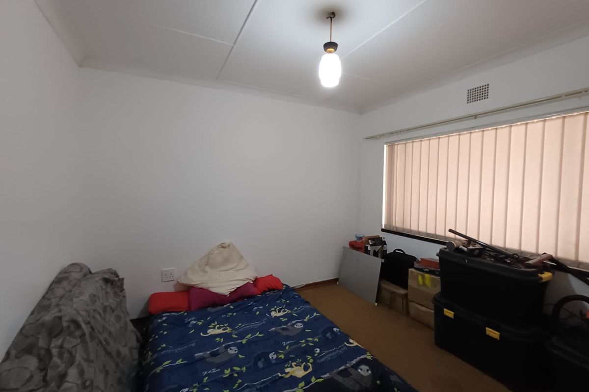 A simple bedroom featuring carpeted flooring, vertical window blinds, and a central ceiling light fixture.