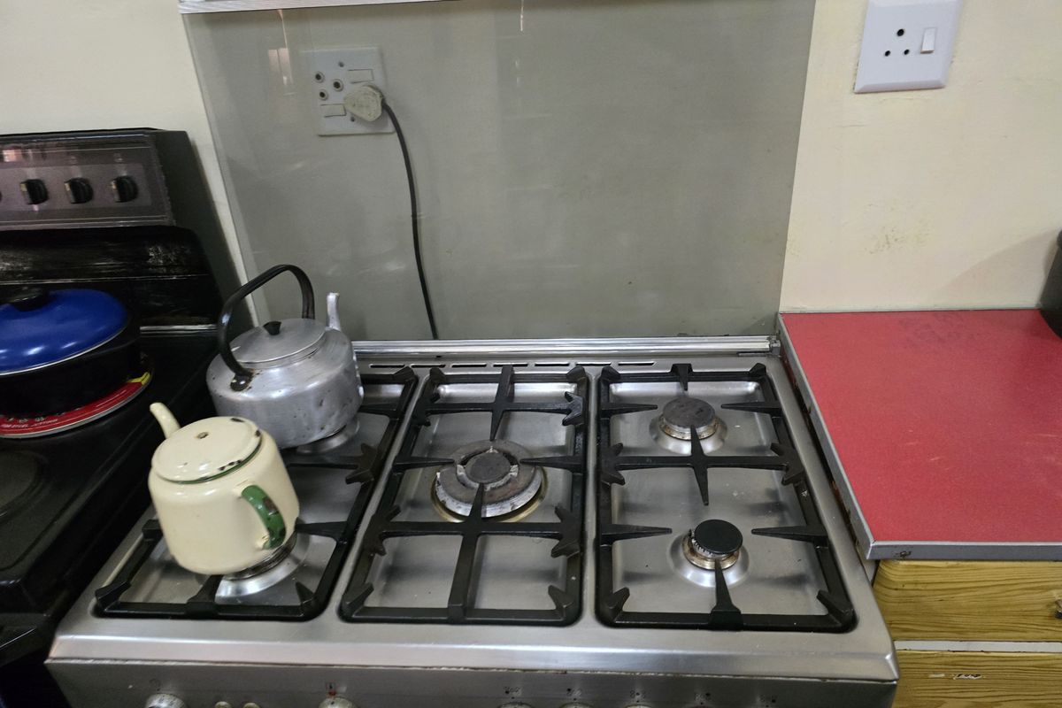 A functional kitchen area featuring a stainless steel gas hob with cast iron grates and a glass splashback.