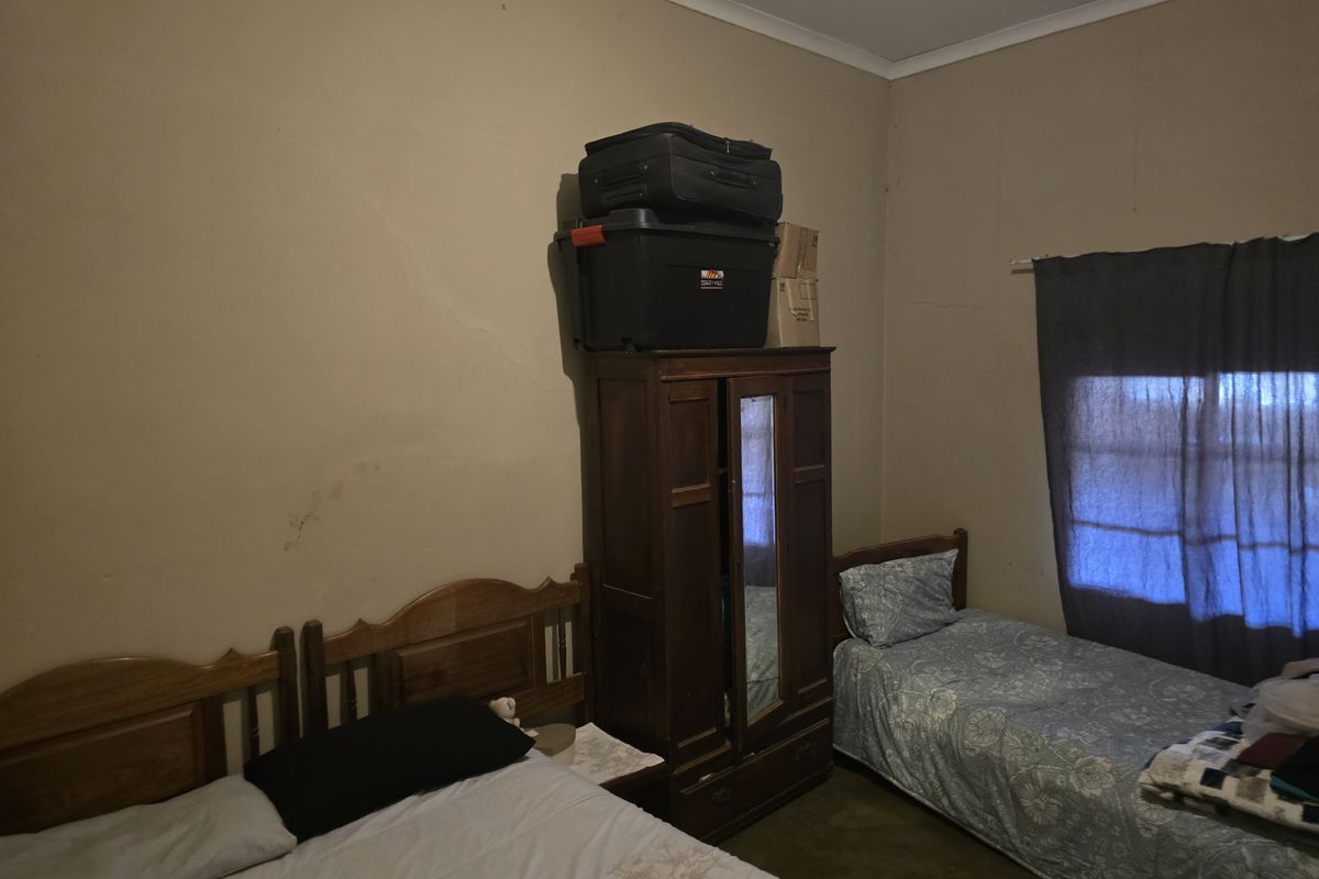 A bedroom featuring two beds and a wooden wardrobe, with visible wall surface wear and aging finishes.