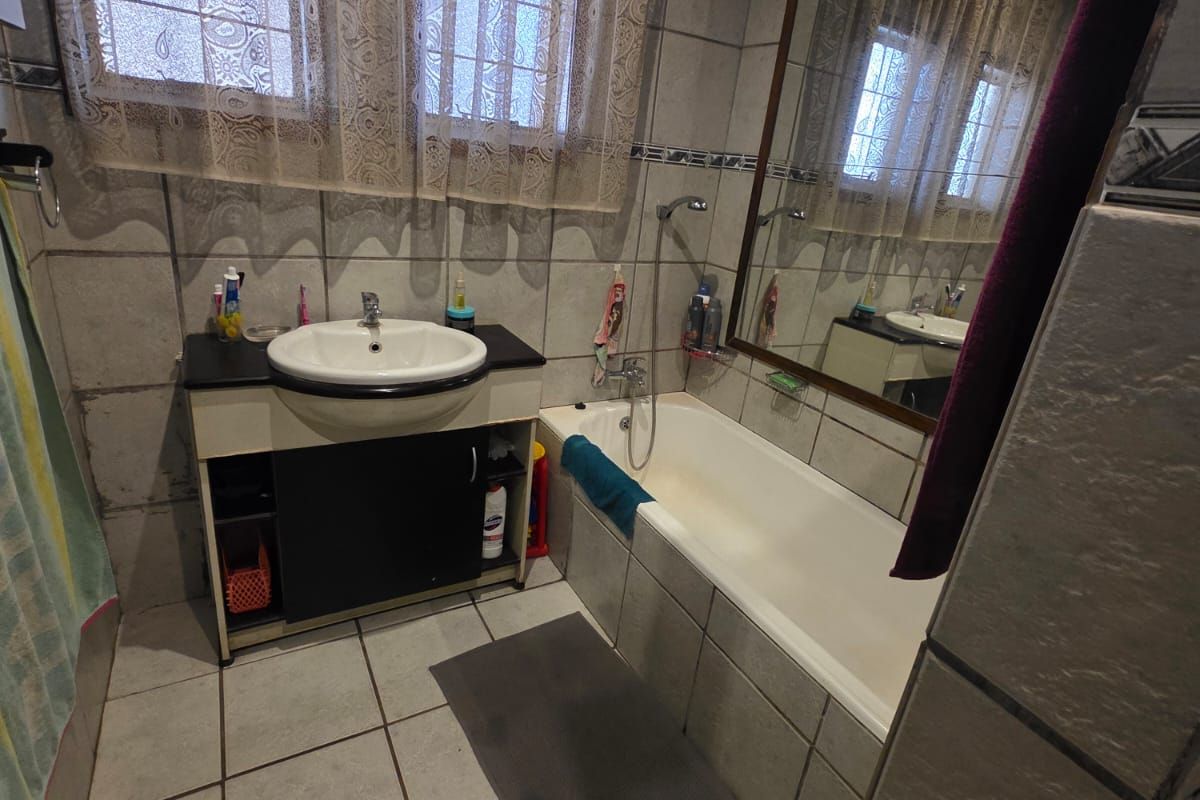 A functional bathroom featuring a built-in vanity with basin, a tiled bathtub with shower mixer, and large wall-mounted mirror.