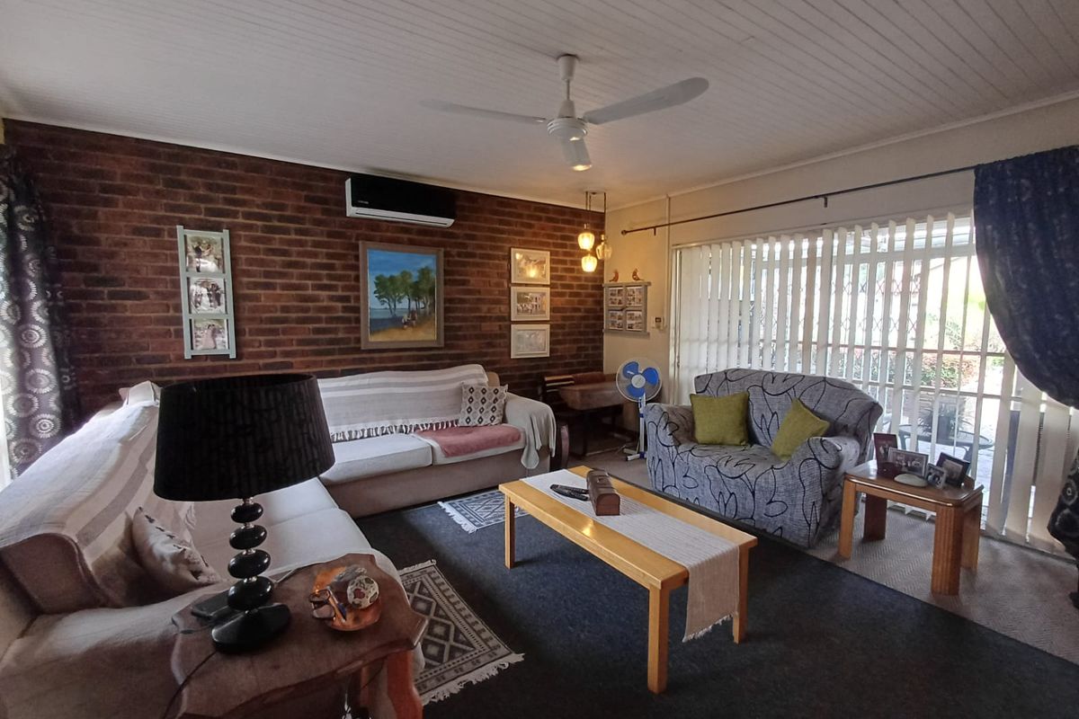 A living room featuring a prominent exposed brick feature wall, a ceiling fan, and a wall-mounted air conditioning unit.