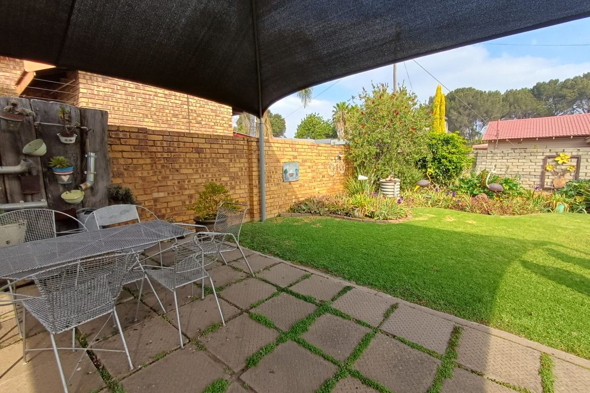 A private rear garden featuring a paved patio area, established lawn, and perimeter brick walling, shaded by a large overhead shade sail.