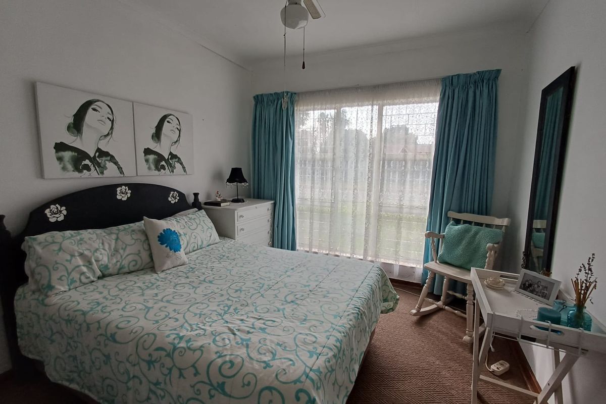 A well-lit bedroom featuring a ceiling fan, carpeted flooring, and large windows with curtains, providing a comfortable and functional living space.