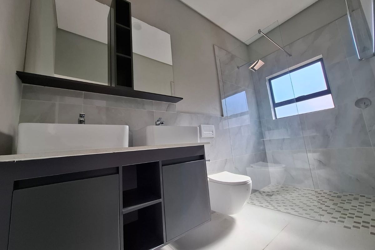 Modern bathroom featuring a double vanity with integrated storage, a wall-hung toilet, and a spacious walk-in shower with glass enclosure and marble-look tiling.