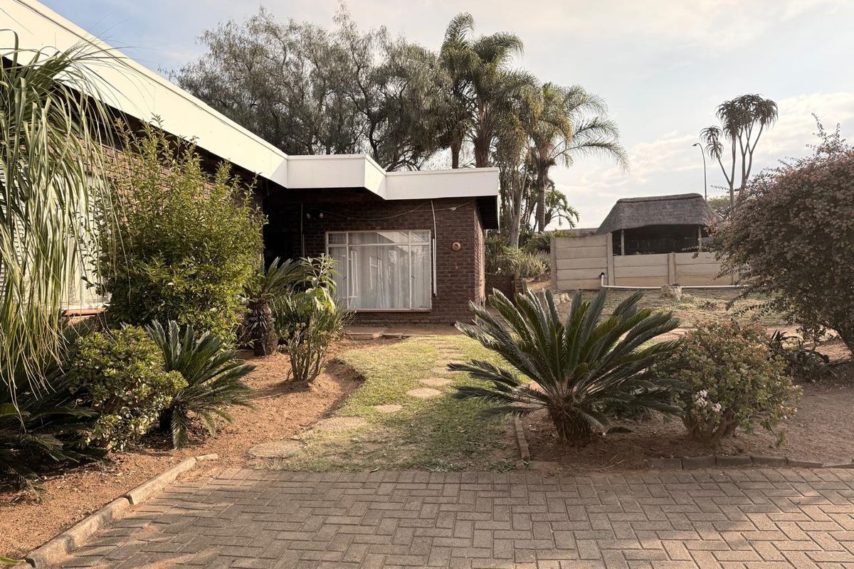 Rear view of the property featuring a brick facade, paved area, and established garden with mature trees and shrubs.
