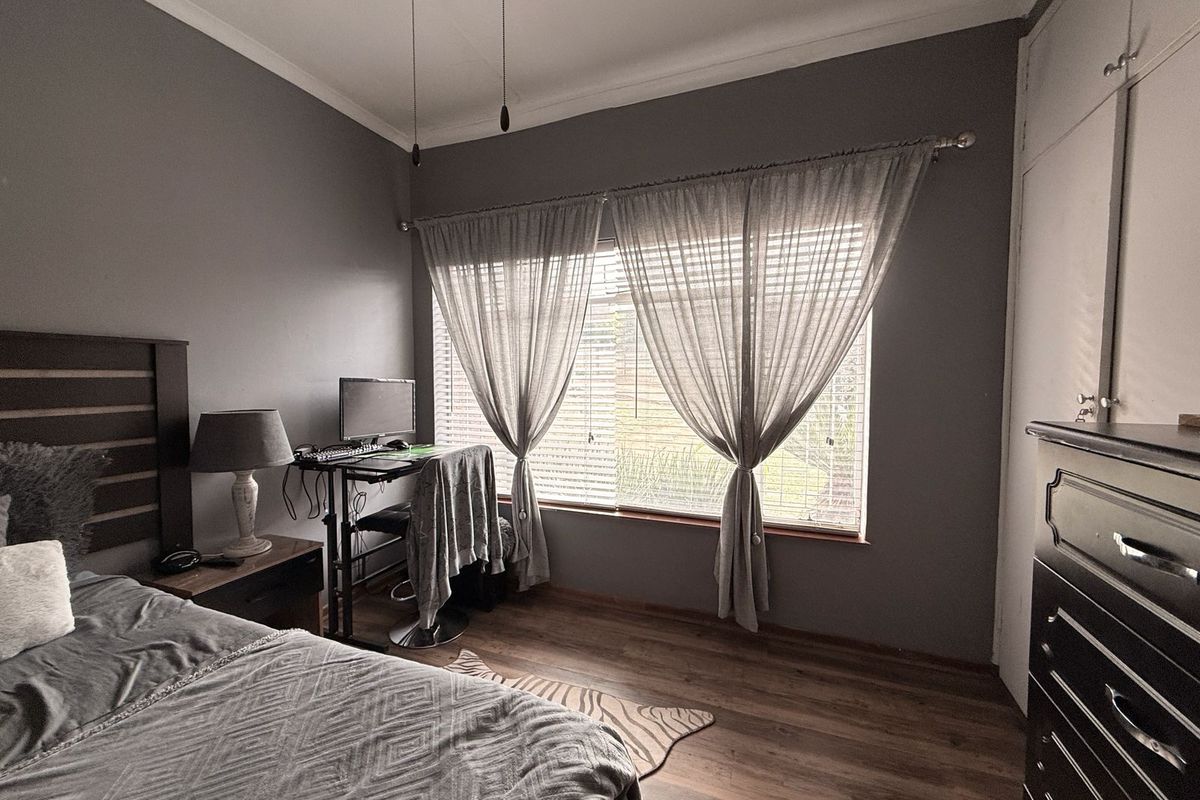 A well-maintained bedroom featuring wood-look flooring, built-in cupboards, and large windows with blinds, offering a comfortable and functional living space.