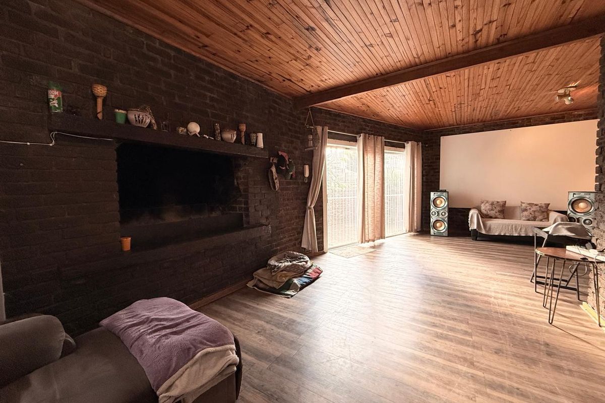 Spacious living area featuring a prominent dark brick fireplace, timber-clad ceiling, and large sliding glass doors providing natural light and garden access.