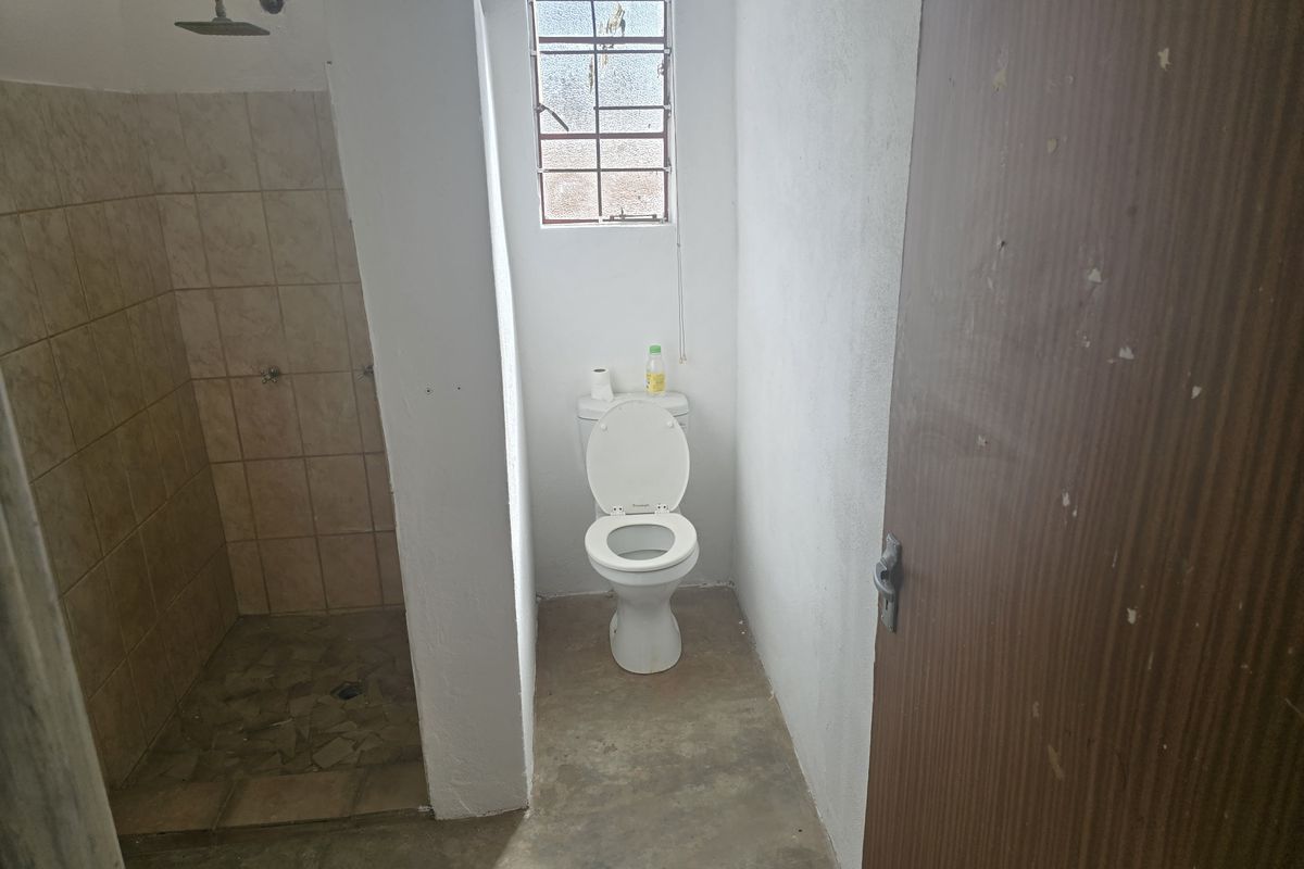 A functional bathroom featuring a walk-in shower with tiled walls and a standard toilet, requiring cosmetic updates to improve the overall finish.
