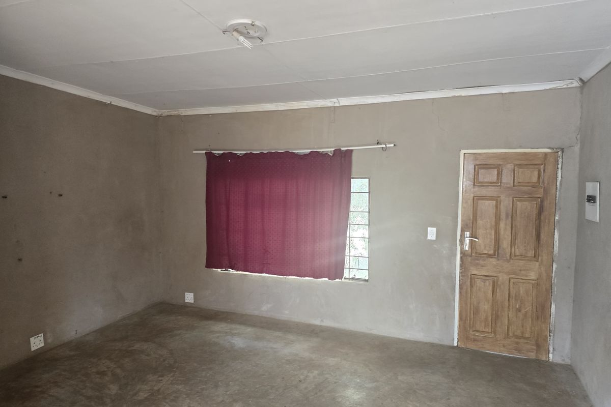 An empty, unfinished room featuring raw plastered walls, a wooden door, and basic electrical fittings, offering a blank canvas for renovation.