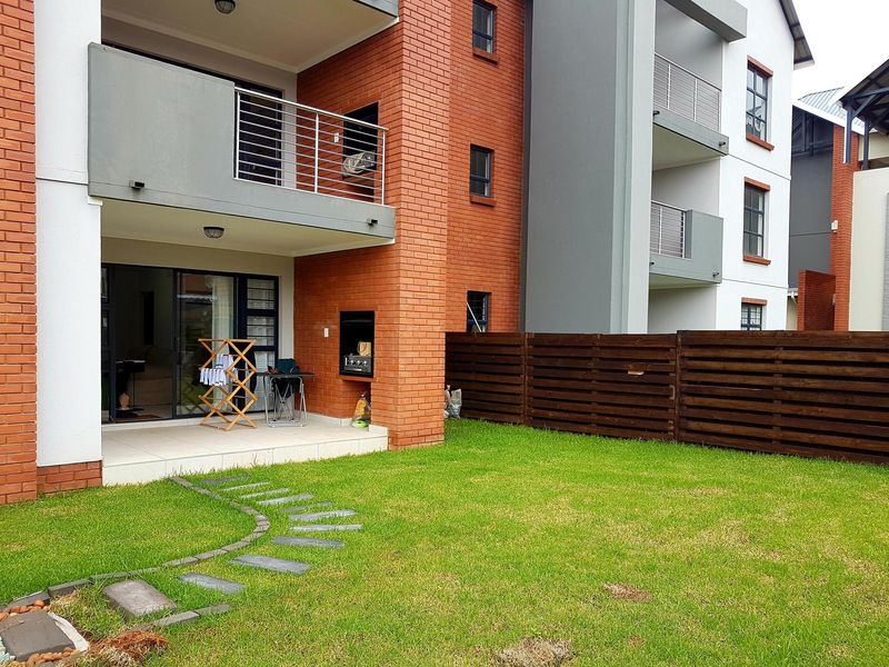 Rear view of the townhouse featuring a private garden, tiled patio with a built-in braai, and an upper-level balcony with metal railings.
