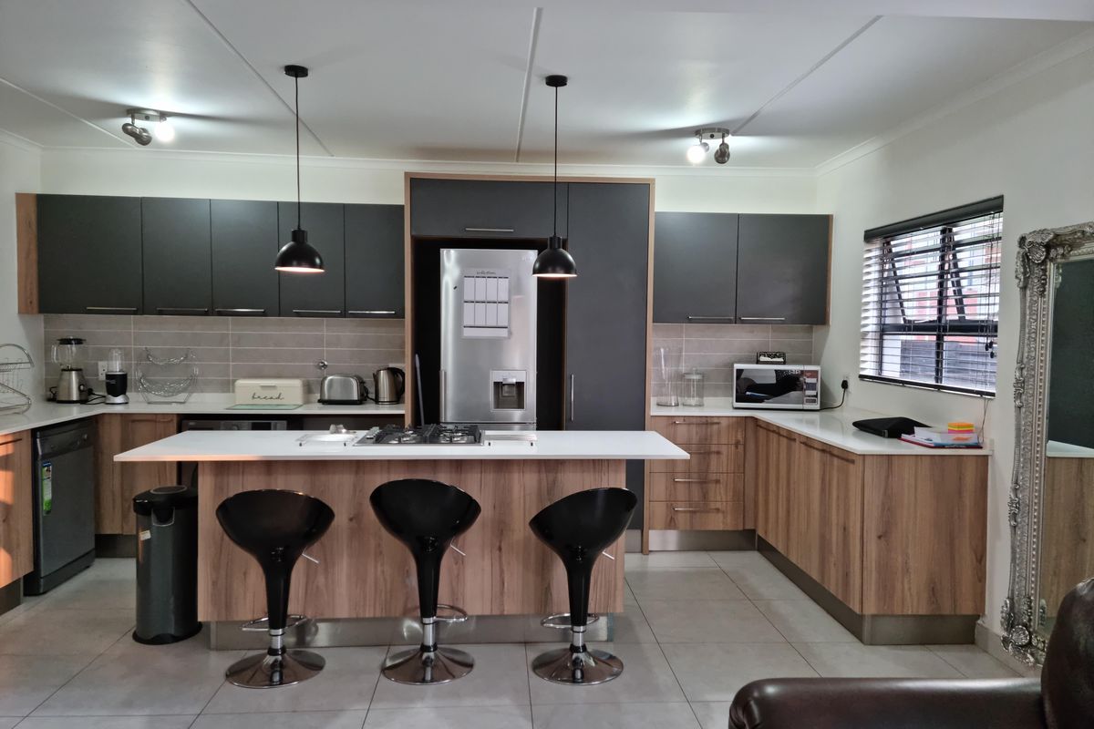 Modern kitchen featuring two-tone cabinetry, a central island with a gas hob, tiled backsplash, and contemporary pendant lighting.