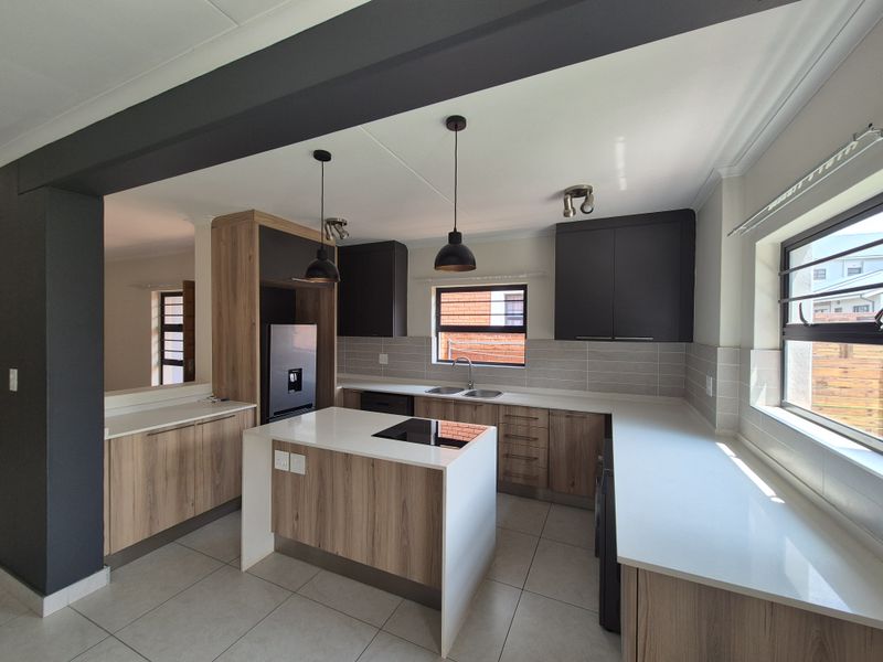 Modern kitchen featuring wood-grain cabinetry, stone countertops, a central island with an integrated cooktop, and contemporary pendant lighting in an open-plan layout.