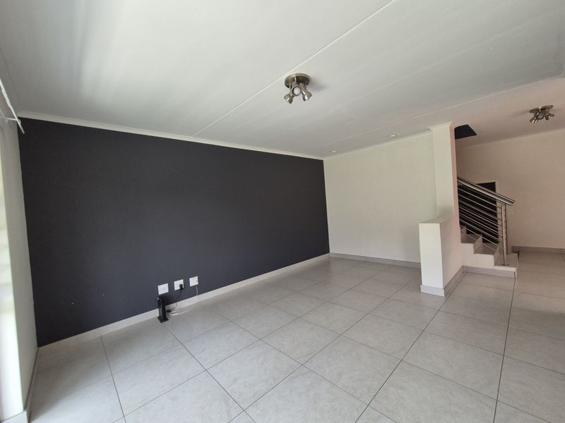 Spacious, empty living area featuring neutral tiled flooring, a modern accent wall, and a staircase with a stainless steel balustrade.
