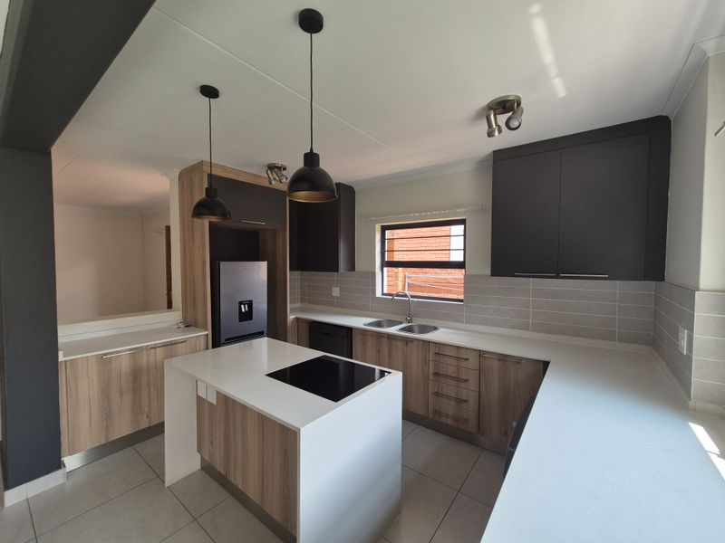 Modern kitchen featuring a central island with an integrated electric hob, stone countertops, ample cabinetry, and contemporary pendant lighting.