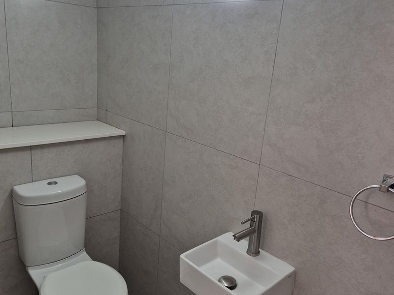 A compact, modern guest bathroom featuring neutral grey wall and floor tiles, a wall-mounted basin, and a standard toilet.