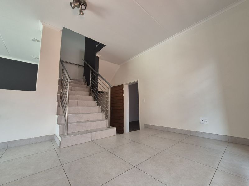An open-plan living area featuring neutral tiled flooring, a modern staircase with stainless steel balustrades, and clean white walls.