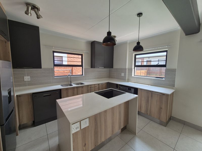 Modern kitchen featuring a central island, quartz countertops, double sink, ample cabinetry, and stylish pendant lighting in a clean, open-plan layout.