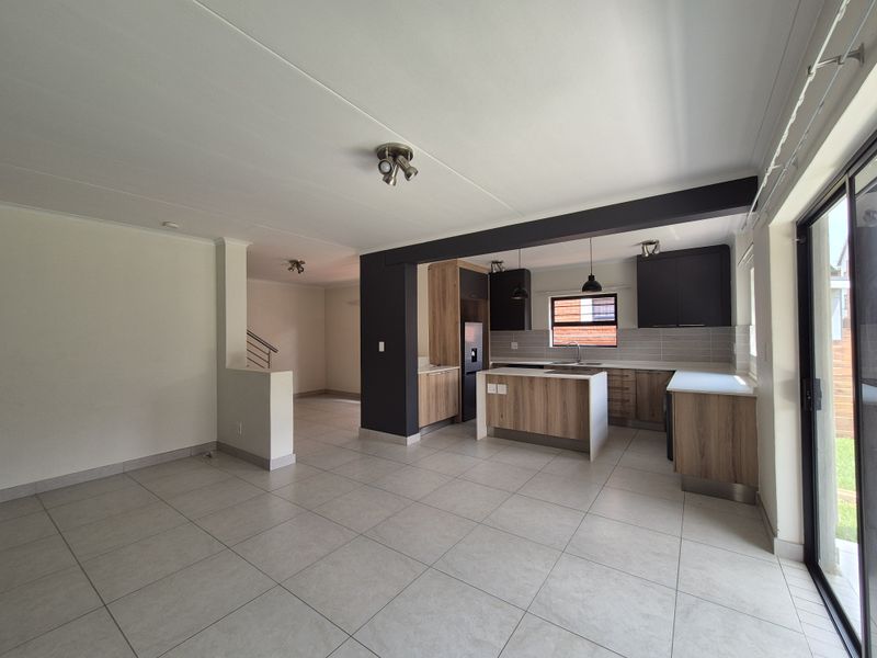 Spacious open-plan living and kitchen area featuring modern wood-finish cabinetry, a central kitchen island, tiled flooring, and direct access to the outdoor space.