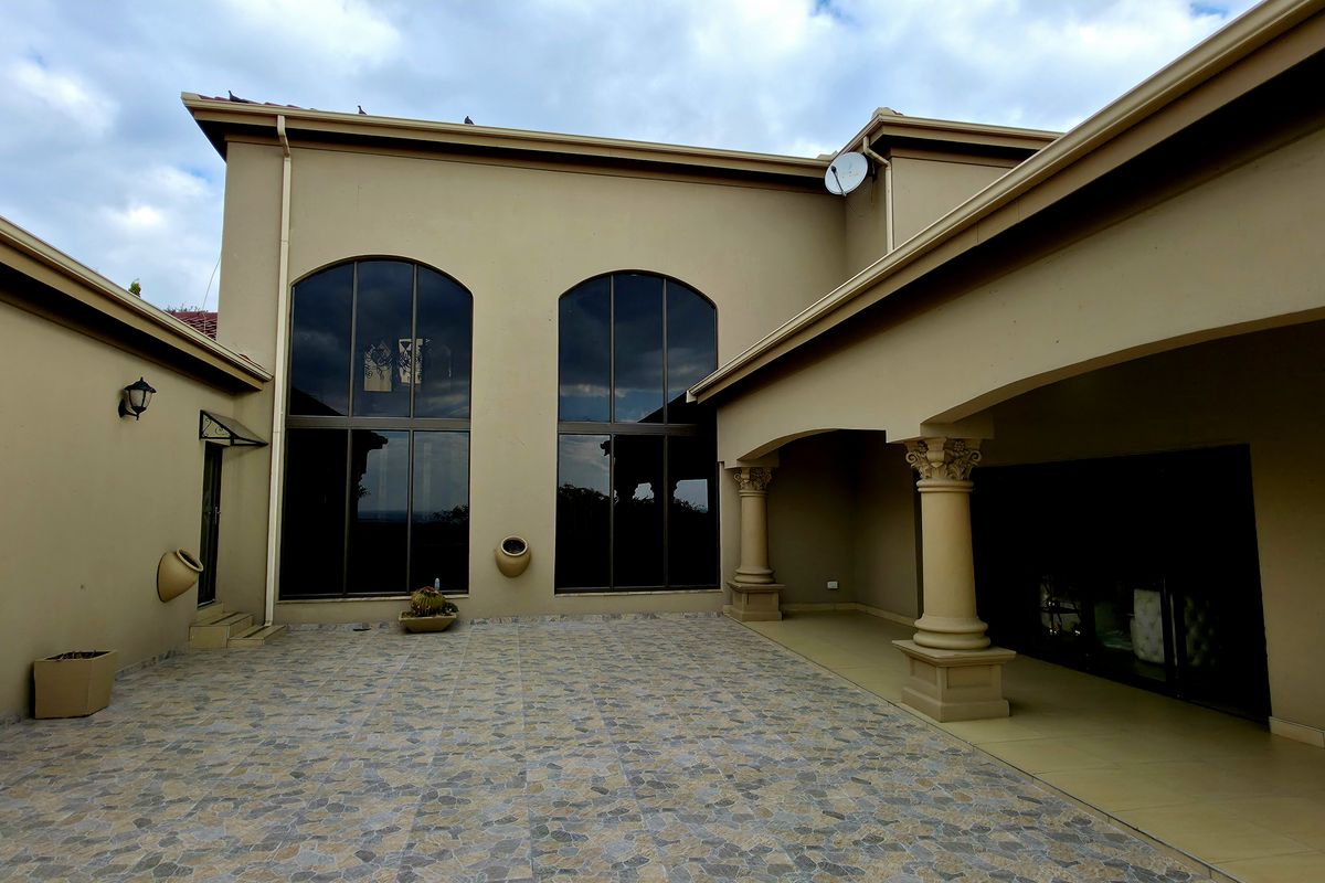 Spacious rear courtyard featuring paved flooring, covered patio area with decorative columns, and large arched windows providing natural light to the interior.