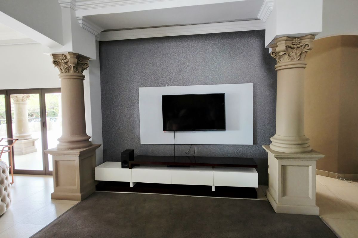 Spacious living area featuring decorative classical columns, a modern feature wall with integrated television mount, and large sliding doors leading to the patio.