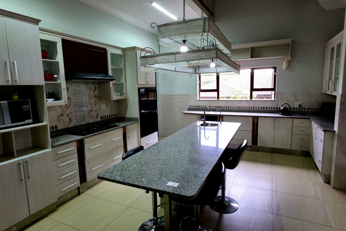 Spacious kitchen featuring granite countertops, a central island with integrated sink, built-in cabinetry, and a dedicated oven and hob setup.