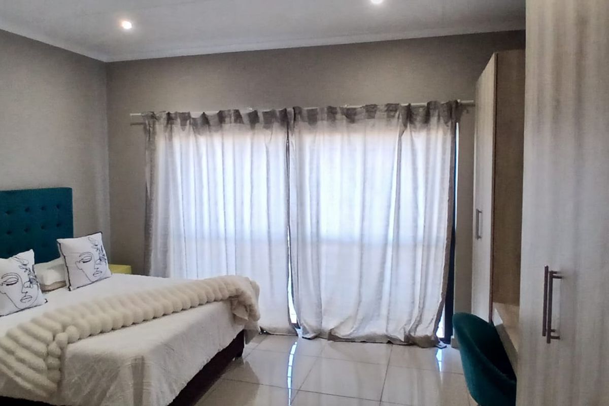 A well-lit bedroom featuring tiled flooring, built-in cupboards, and large sliding doors with curtains leading to an outdoor area.