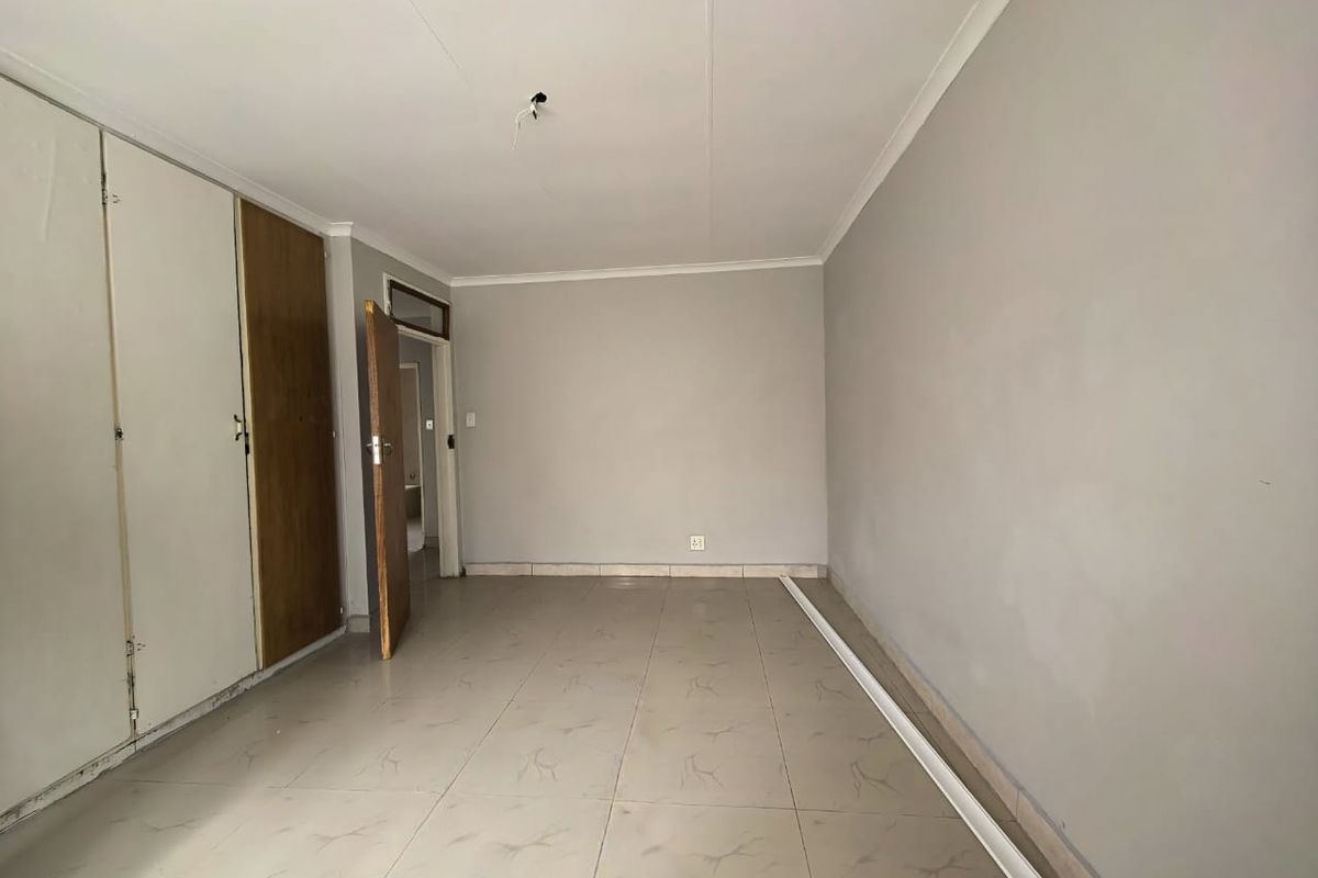 An empty bedroom featuring tiled flooring, built-in cupboards, and neutral wall finishes, awaiting final touches and lighting installation.