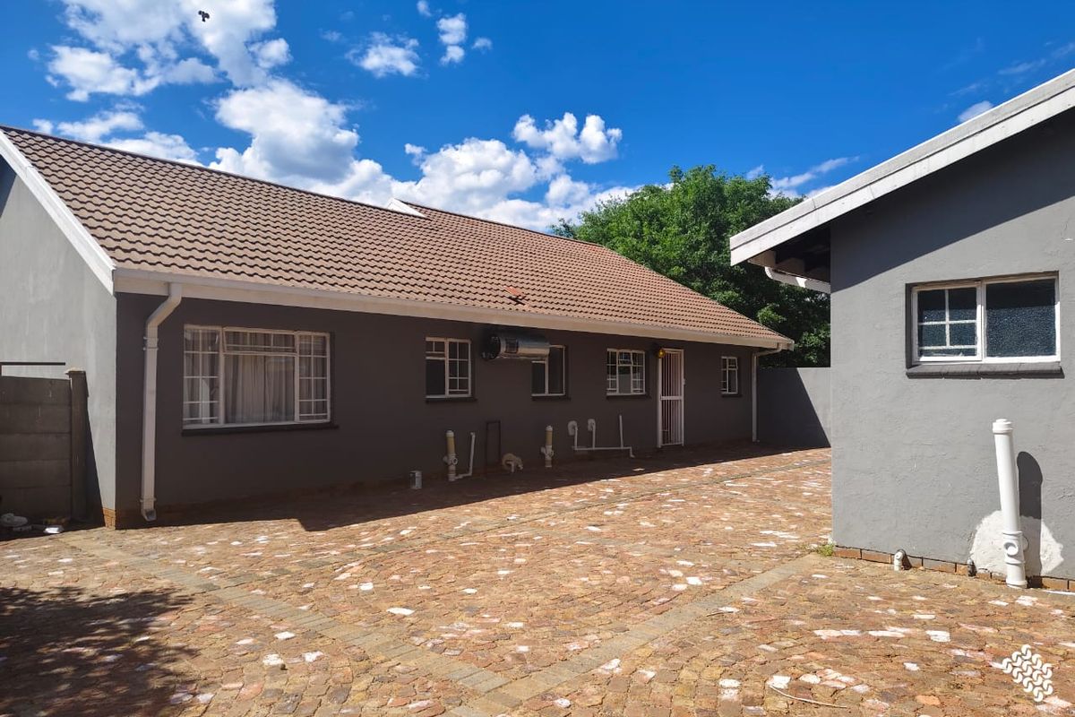 Rear exterior view of the property featuring a paved courtyard, tiled roof, and visible exterior plumbing fixtures.