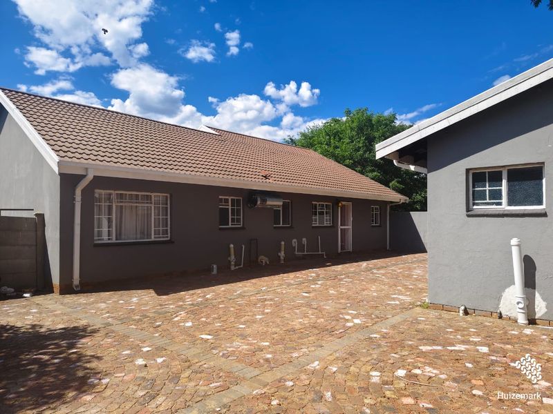 Rear exterior view of the property featuring a paved courtyard, tiled roof, and visible exterior plumbing fixtures.
