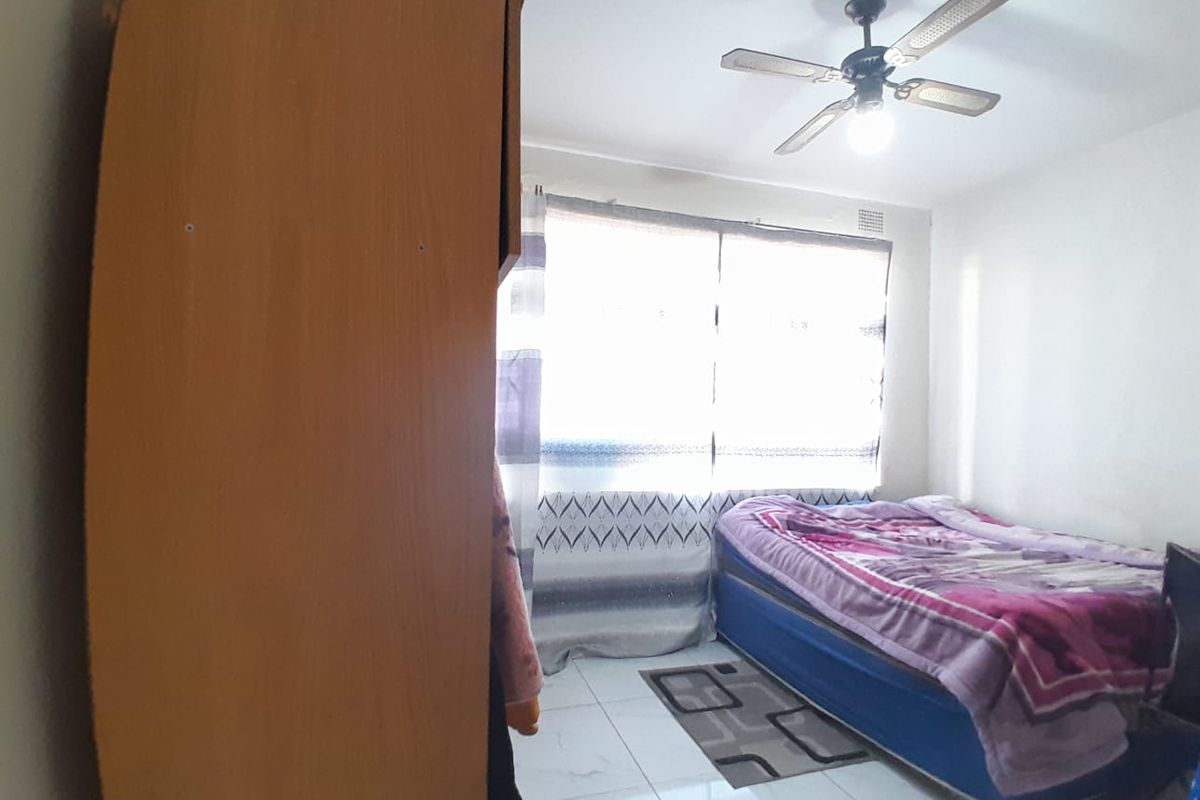 A bedroom featuring tiled flooring and a ceiling fan, providing a functional living space with natural light.