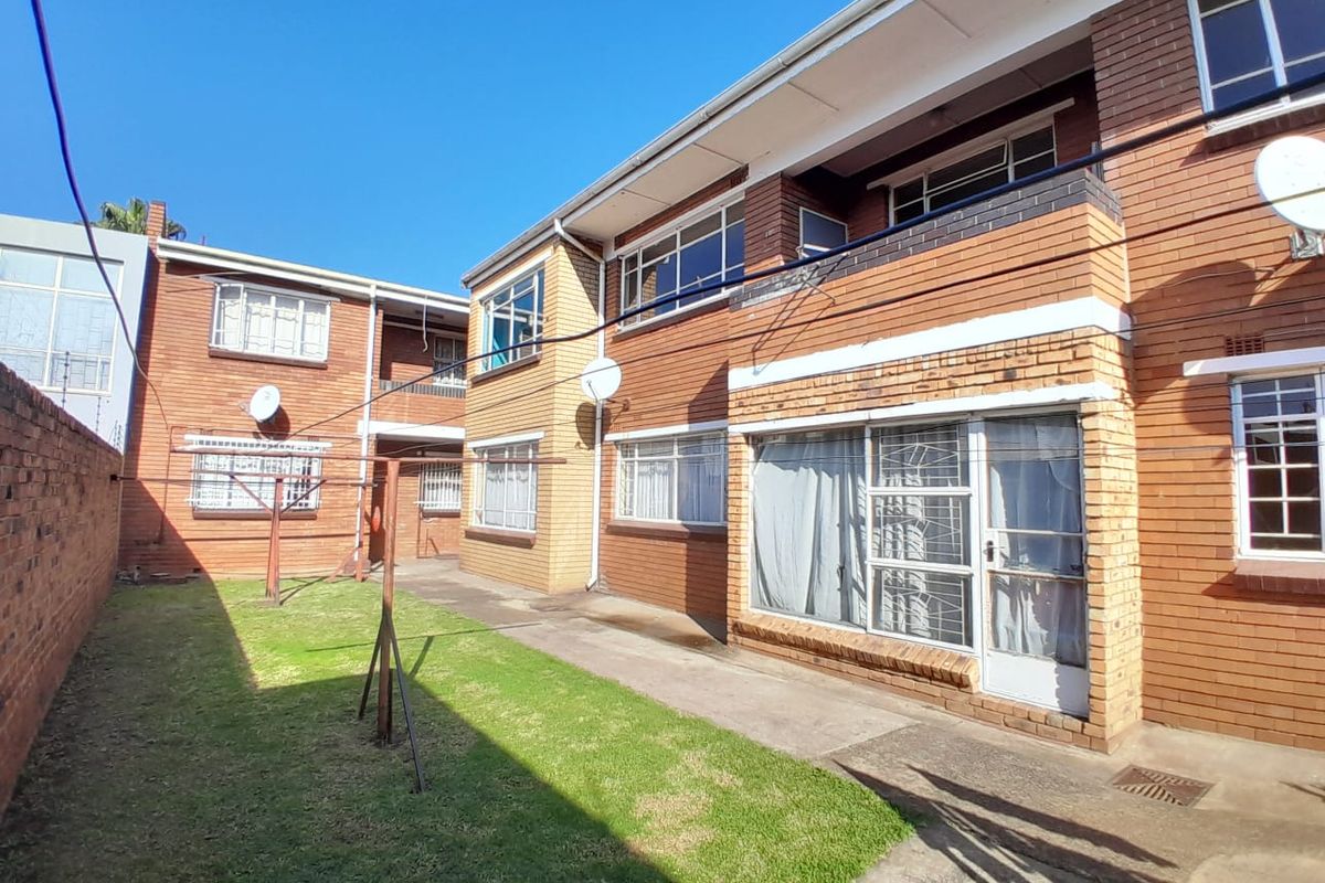 Rear view of a brick apartment building featuring a shared garden area, paved walkway, and security-barred windows.