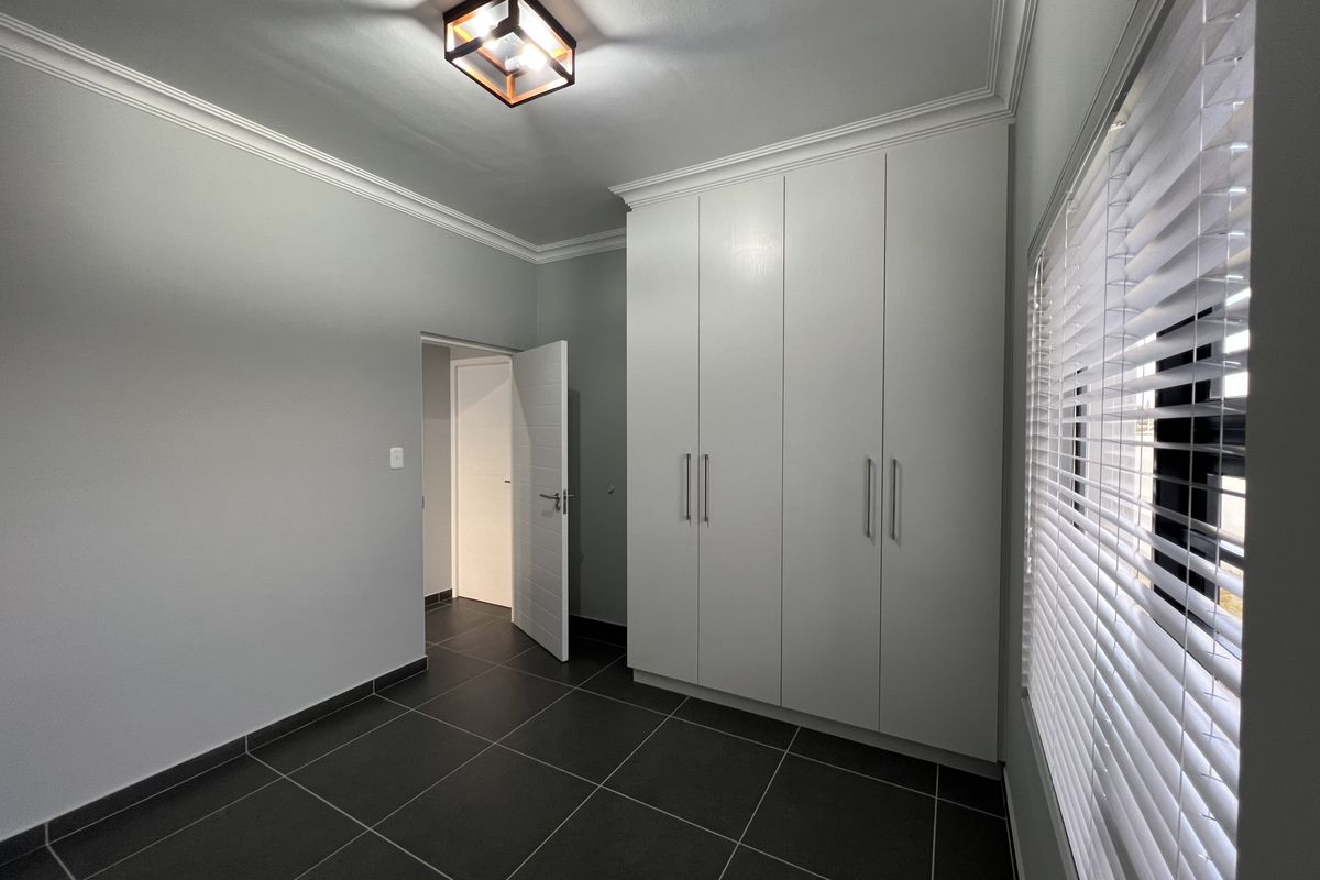 A clean, modern bedroom featuring neutral grey walls, dark tiled flooring, and ample built-in cupboard storage with contemporary finishes.