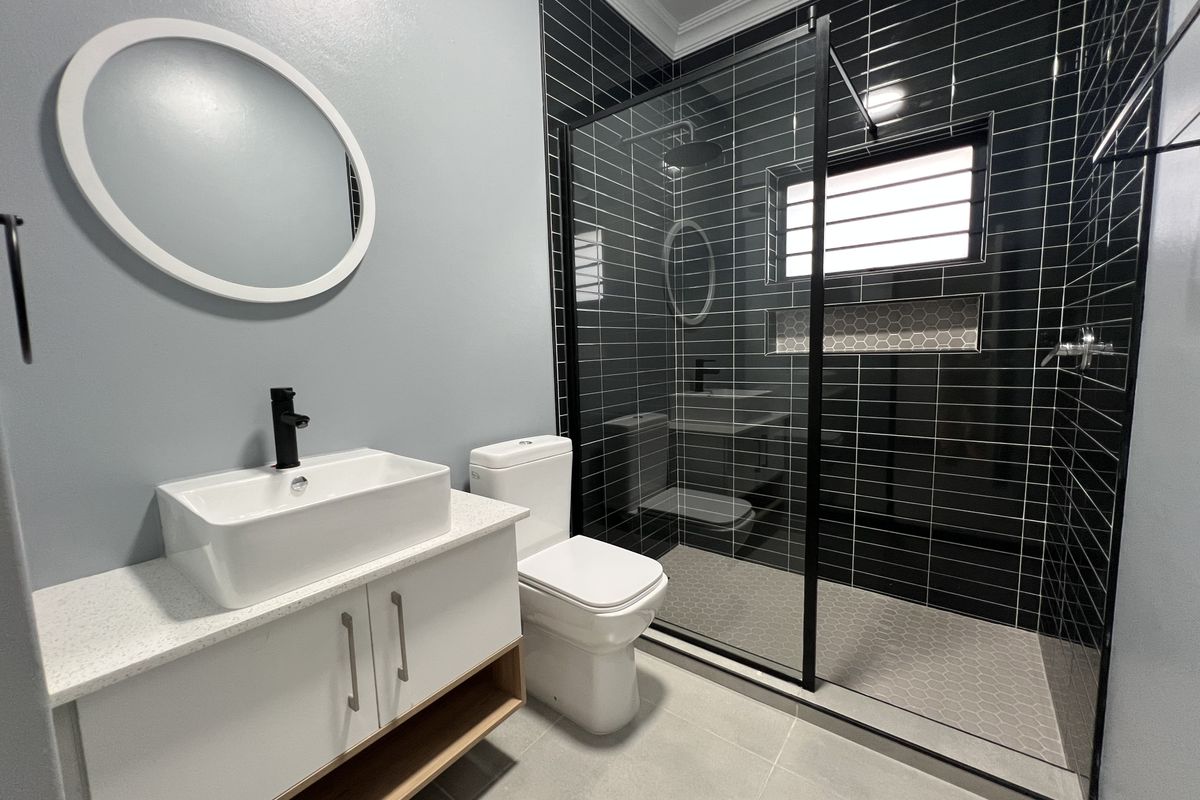 Modern bathroom featuring a white vanity with vessel sink, black fixtures, and a spacious walk-in shower with black-framed glass enclosure and tiled finishes.