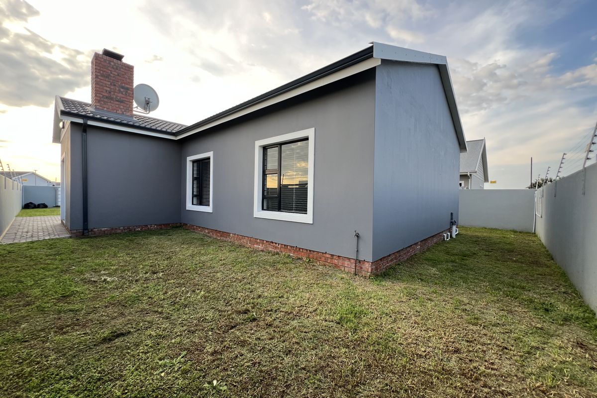 Rear view of the property featuring a modern grey facade, brick chimney, and a private garden enclosed by perimeter walls with electric fencing.