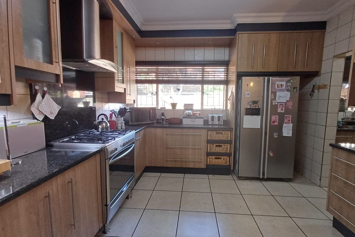 A functional kitchen featuring wood-finish cabinetry, granite countertops, a gas stove with extractor fan, and tiled flooring.