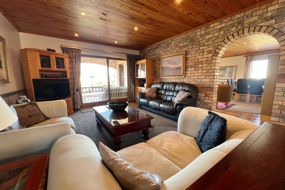 Spacious living room featuring a rustic timber-paneled ceiling, exposed brick feature wall, and sliding glass doors leading to an outdoor patio area.