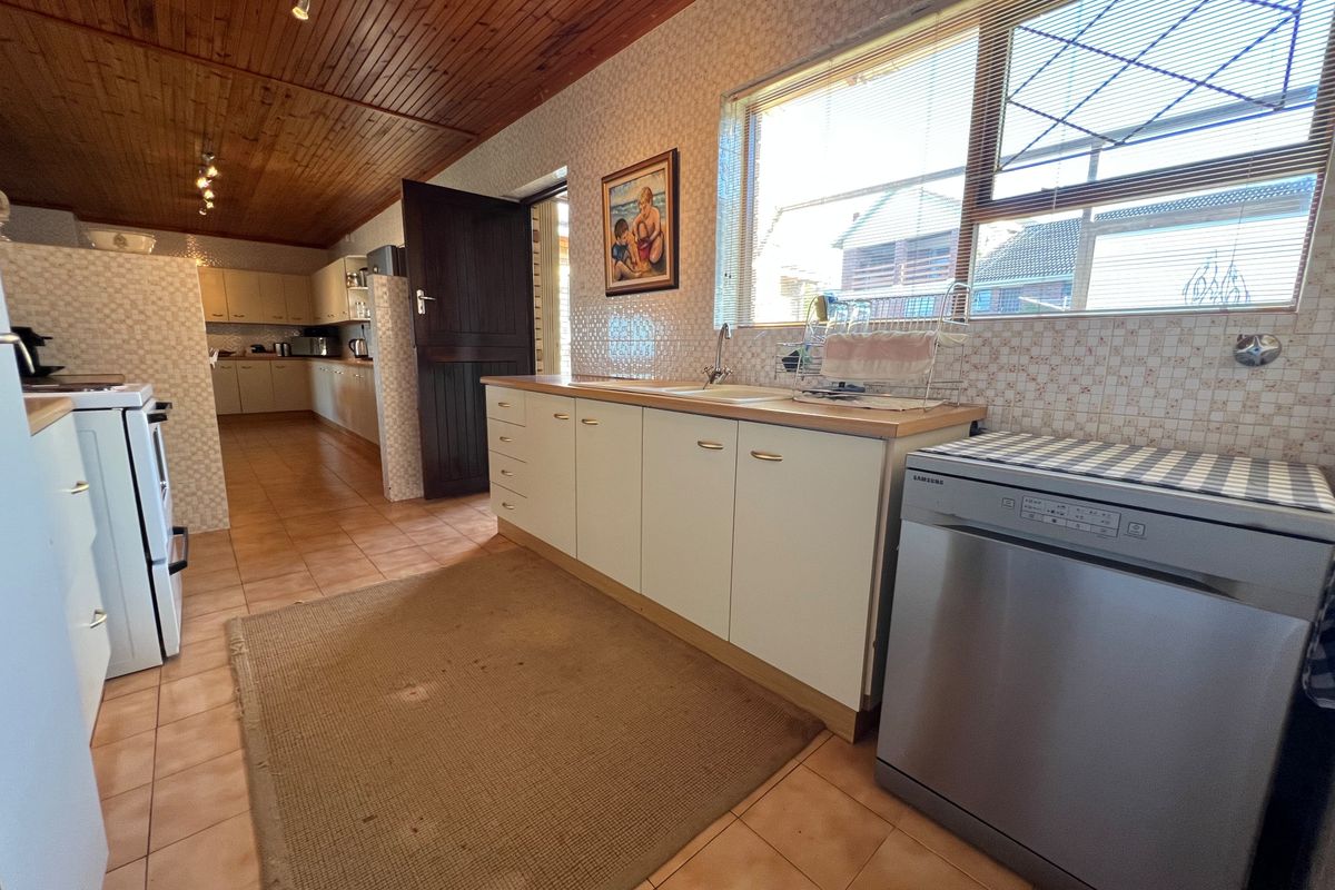 Spacious kitchen featuring timber ceiling, tiled flooring, ample cabinetry, and a double sink, offering a functional layout with potential for modernization.