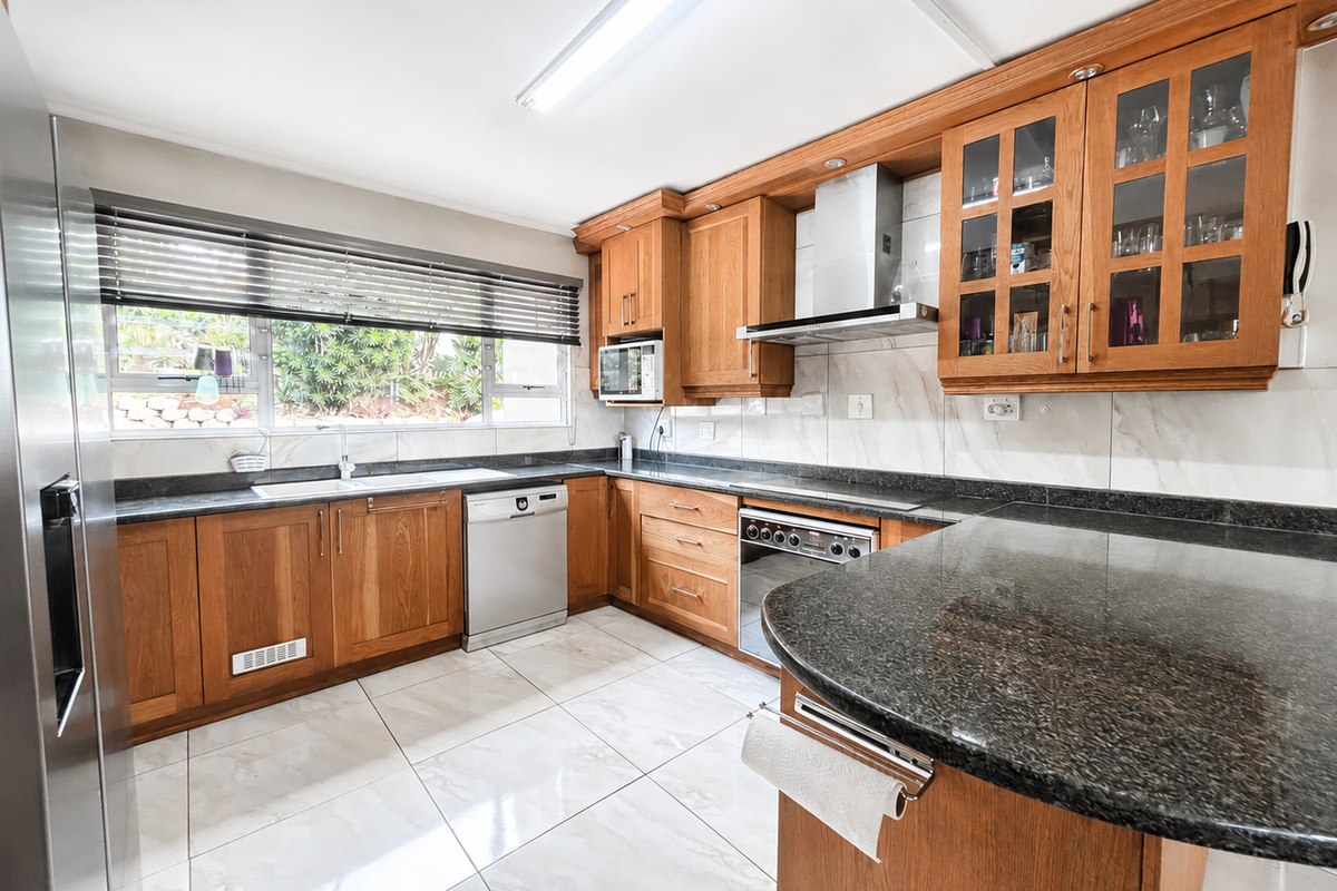 A well-maintained kitchen featuring warm timber cabinetry, dark granite countertops, a stainless steel extractor fan, and polished floor tiles.