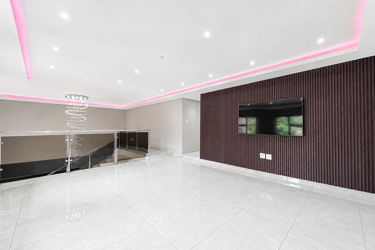 Spacious living area featuring polished porcelain floor tiles, a modern slatted feature wall, recessed LED strip lighting, and a glass balustrade staircase.