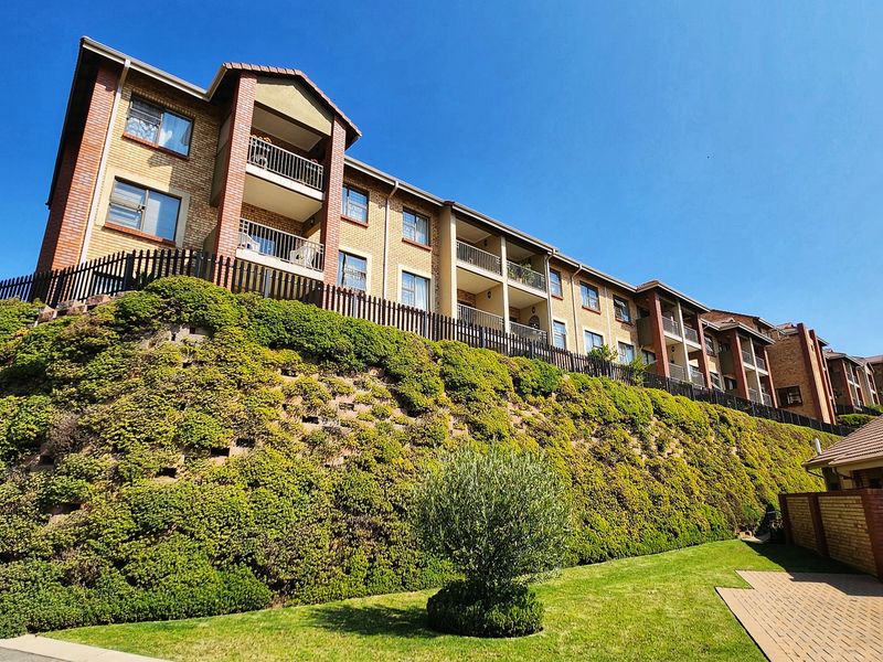 Exterior view of a multi-story apartment complex featuring brick facades, private balconies, and a well-maintained landscaped retaining wall and garden area.