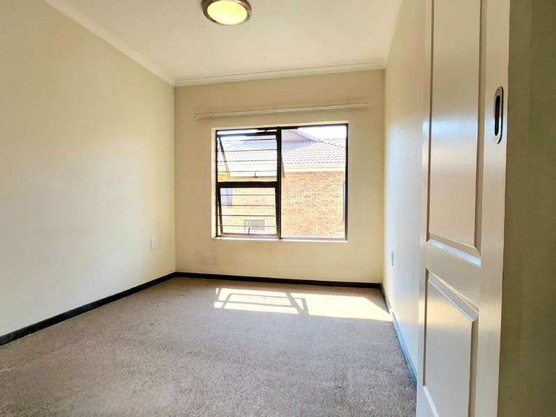 An empty bedroom featuring carpeted flooring, a window with security bars, and neutral wall finishes.