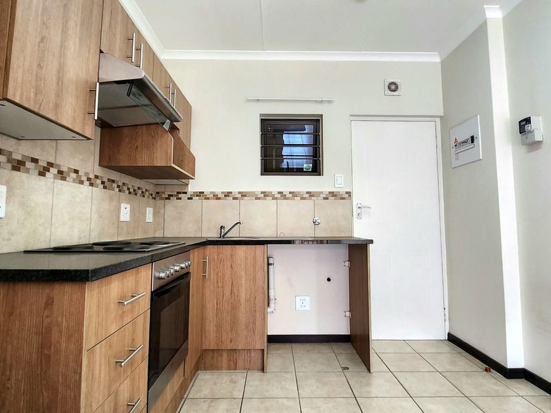 A functional kitchen featuring wood-look cabinetry, dark countertops, built-in oven and hob, tiled backsplash, and tiled flooring.