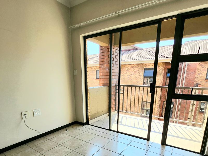 An empty living room featuring tiled flooring and large sliding glass doors that open onto a private balcony.