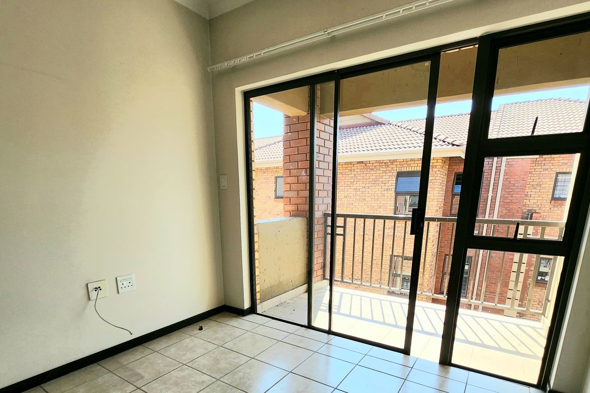 An empty living room featuring tiled flooring and large sliding glass doors that open onto a private balcony.