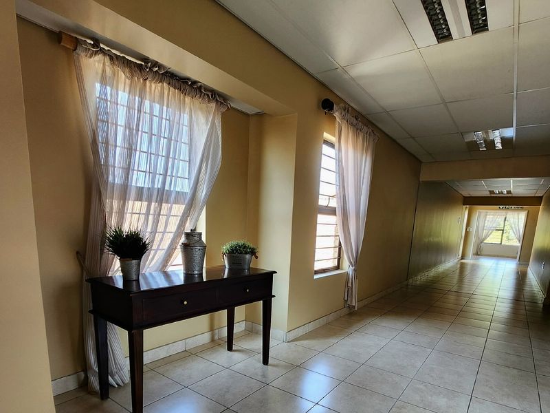 A long, tiled hallway featuring a suspended ceiling, recessed lighting, and security bars on the windows, providing access through the apartment.