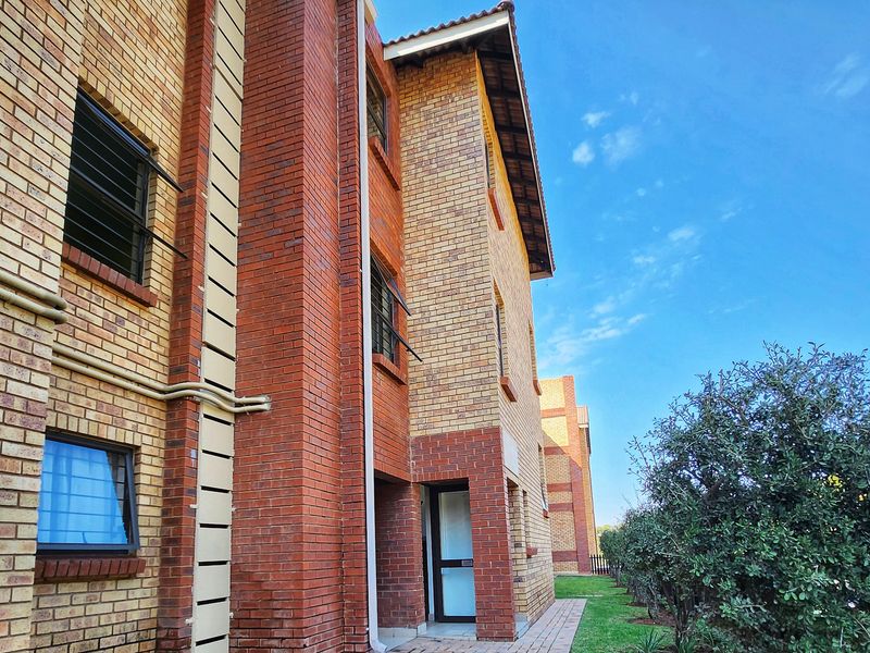 A view of the apartment complex exterior featuring face brick construction, tiled roofing, and a paved walkway leading to the entrance.